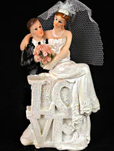 свадебная фигурка для торта невеста, сидящая на постаменте с надписью LOVE и стоящий рядом жених, фото